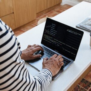 A senior adult programmer coding at home on a laptop, showcasing a work-from-home setup.