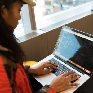 A focused woman typing code on her laptop indoors, embodying tech innovation.
