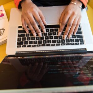 Close-up of hands typing on a laptop keyboard, Python book in sight, coding in progress.