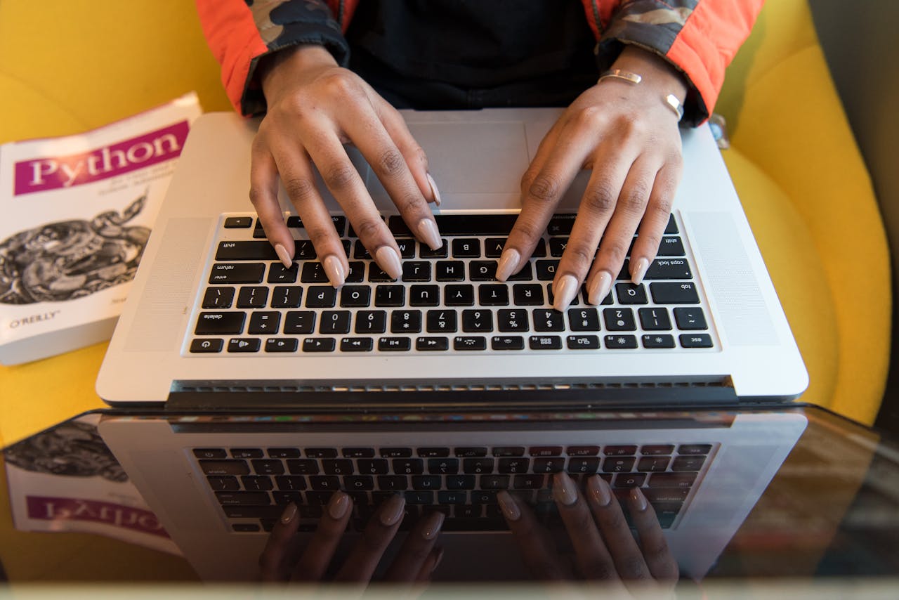 our-stories A person typing on a laptop with a Python programming book visible, capturing technology and learning.