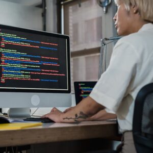 Woman programming at desk with multiple monitors in a modern office setting.