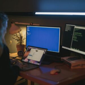 Woman using multiple screens for cybersecurity tasks in a cozy home office