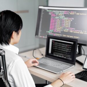 A software developer working on code with multiple screens in a modern office setting.