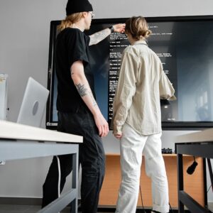 Two young adults collaborating on a coding project in a modern office setting.