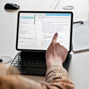 A person pointing at a code script on a tablet, emphasizing modern programming techniques.